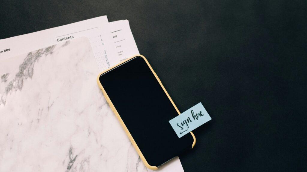 Smartphone auf Dokumenten mit Notiz «sign here» – qualifizierte elektronische Signatur (QES)